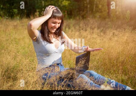 giovane donna adulta guarda un laptop in un panico e tiene la testa. problema di rete. shock contenuto Foto Stock