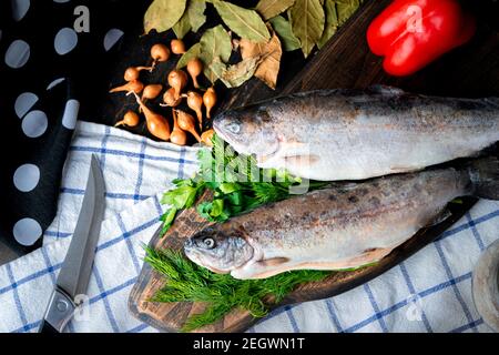 Due trote arcobaleno grezze con guarnitura su tavola di legno. Foto Stock