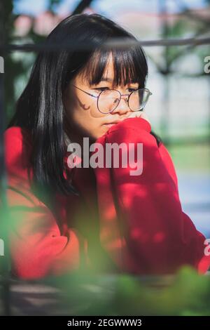 un adolescente asiatico che indossa un pullover rosso seduto all'aperto Foto Stock