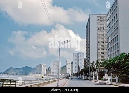 Guardando verso ovest lungo Avenida Marechal Deodora da Fonseca a Guarujá, São Paulo, Brasile 1961. Alti blocchi di appartamenti iniziano a dominare la scena fronte spiaggia anche nei primi anni '60. Guarujá si trova sull'isola di Santo Amaro, nello stato di São Paulo. Questo nome deriva dalla lingua Tupi, e significa ‘percorso stretto’. Questa immagine proviene da una vecchia trasparenza di colore dilettante da 35 mm. Foto Stock