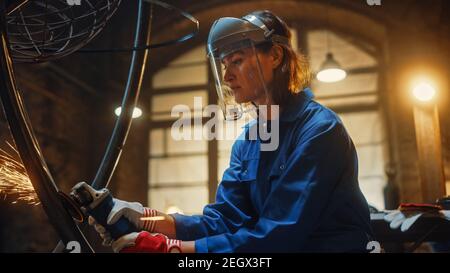 Primo piano Ritratto di bella Femminile Fabricator in maschera di sicurezza. Sta macinando un oggetto metallico e Flying Hot Sparks riflettere sulla maschera. Potenziamento Foto Stock