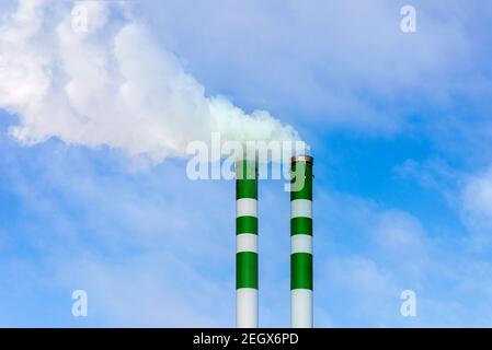 Due tubi industriali di fumo da camino su cielo blu nuvoloso.il fumo bianco emana dai tubi. Foto Stock