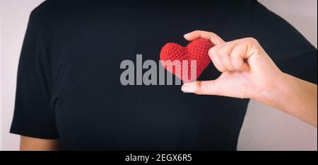 Mani che tengono il cuore rosso su sfondo nero isolato, copy space, concetto di amore, speranza, assistenza sanitaria, donazione di organi, assicurazione e CSR, giornata del cuore mondiale, Foto Stock