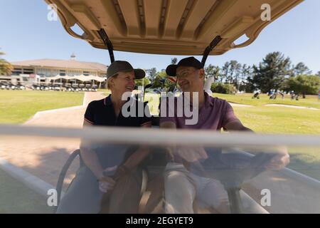 Uomo e donna caucasica che guida golf buggy sul golf naturalmente parlando e sorridendo Foto Stock