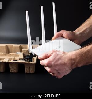 Mani maschili disimballare il nuovo router WiFi su sfondo nero. Foto Stock