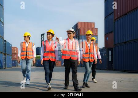Il caposquadra asiatico cammina e spiega le varie operazioni nel terminal dei container con quattro nuovi apprendisti. Foto Stock