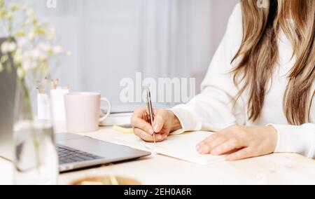 Donna scrive nel notebook sulla scrivania con il computer portatile Foto Stock
