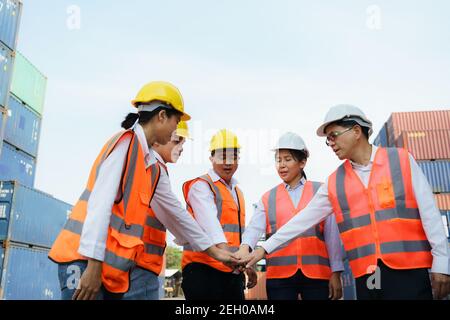 Il caposquadra asiatico e il suo lavoratore di squadra stanno tenendo insieme le mani al terminale del deposito del contenitore per l'unità e il concetto di successo. Foto Stock