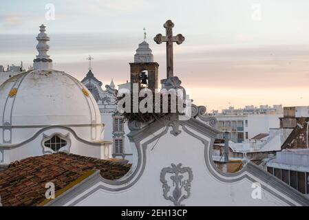 Nido di cicogna e torri della chiesa principale della città Olhao, Portogallo all'alba Foto Stock
