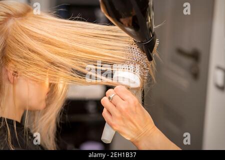 Primo piano della mano del parrucchiere è l'asciugatura dei capelli del giovane donna bionda in un parrucchiere Foto Stock