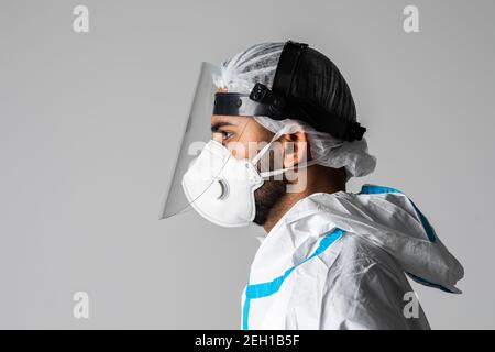 Ritratto di medico uomo che indossa googles, occhiali protettivi in tuta di protezione, maschera chirurgica viso su sfondo bianco. Foto Stock