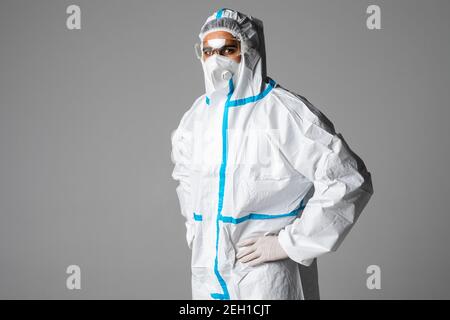 Ritratto di medico uomo che indossa googles, occhiali protettivi in tuta di protezione, maschera chirurgica viso su sfondo bianco. Foto Stock