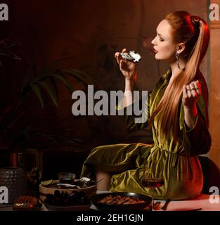 Una ricca donna dai capelli rossi è seduta sul tavolo, servita con ostriche, frutti di mare e vino che mangiano grandi ostriche dell'Atlantico Foto Stock