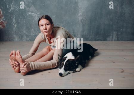 Donna adulta matura che fa yoga a casa in soggiorno con cane di corgi Foto Stock