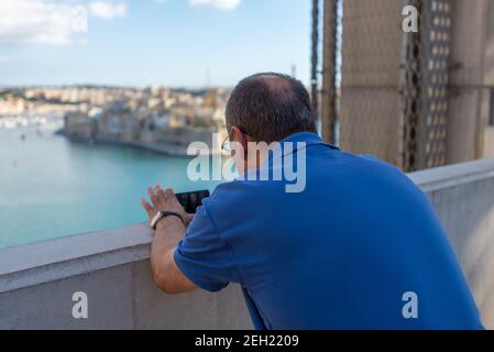 Uomo in camicia blu che scatta foto con il suo cellulare Foto Stock