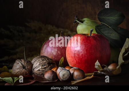 noci e frutta con fogliame in stile rustico al buio sfondo di legno Foto Stock