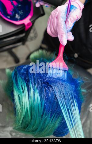 Ripresa ad alto angolo dei capelli di tintura di processo in salone di bellezza. Parrucchiere in guanto protettivo con spazzola magenta mentre si applica vernice blu ai capelli della donna Foto Stock