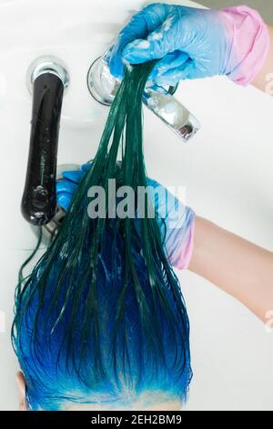 Foto ad alto angolo di parrucchiere in guanti shampooing testa del cliente con capelli lunghi colore zaffiro dopo tintura capelli processo. Lavaggio dei capelli della donna Foto Stock