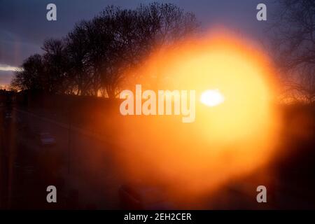 La calda luce arancione di un tramonto in ritardo, che splende attraverso la condensazione, si illumina in una finestra che si affaccia su una strada residenziale e su alti alberi a sud di Londra, il 12 febbraio 2021, a Londra, Ebngland. Foto Stock