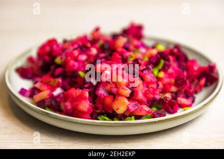 Insalata russa di barbabietole di vinegret di verdure bollite in piatto bianco grigio su sfondo bianco della tavola. Foto Stock