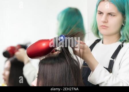 Lady capelli stylist che asciugano i capelli della brunetta con l'asciugacapelli rosso e. spazzola blu nel salone di bellezza Foto Stock