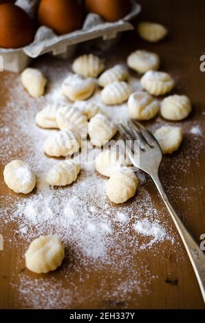 Gnocchi freschi fatti in casa non cotti su una tavola di legno infarinato con una forchetta e alcune uova in una scatola di uova. Foto Stock