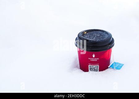 Mosca. Russia. 19 febbraio 2021. Primo piano della tazza di carta rossa nella neve bianca. Sul coperchio della tazza sono presenti fiocchi di neve. All'interno della tazza è disponibile un contenitore monouso Foto Stock