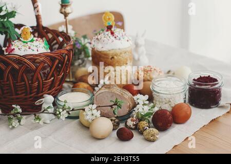 Cibo pasquale tradizionale per la benedizione, pane pasquale fatto in casa, uova di pasqua eleganti e fiori di primavera fioritura su tovagliolo di lino su tavola rustica. Felice EA Foto Stock