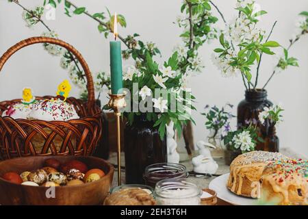 Cibo pasquale tradizionale per la benedizione, pane pasquale fatto in casa, uova di pasqua alla moda, candela e fiori di primavera in fiore su tovagliolo di lino su tavola rustica. Foto Stock