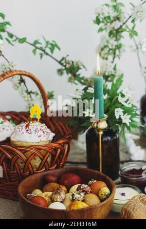 Cibo pasquale tradizionale per la benedizione, pane pasquale fatto in casa, uova di pasqua alla moda, candela e fiori di primavera in fiore su tovagliolo di lino su tavola rustica. Foto Stock