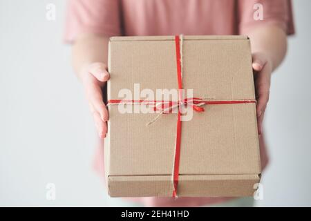 Messa a fuoco selezionata. Ragazza che tiene una scatola di regalo con un nastro rosso nelle sue mani Foto Stock