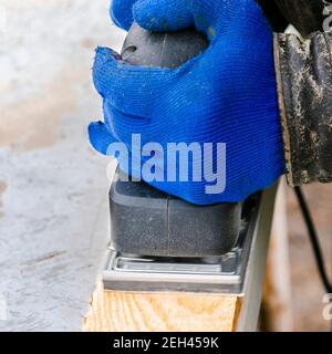 Lavorare con una macchina smerigliatrice. Le mani degli uomini in guanti blu funzionano con utensili elettrici Foto Stock
