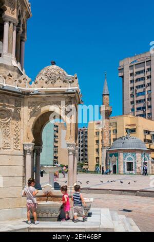 Smirne, provincia di Smirne, Turchia. Piazza Konak. La Moschea di Konak vista dalla Torre dell'Orologio che è in parte vista sulla sinistra, dove tre bambini sono pla Foto Stock