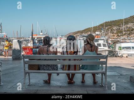 Komiza, Croazia - 16 agosto 2020: I turisti siedono sulla panchina di fronte al porto della città vecchia Foto Stock