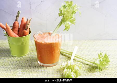 Un bicchiere spremuto di succo vegetale sano dalle carote e un secchio di carote su un tovagliolo verde. Foto Stock