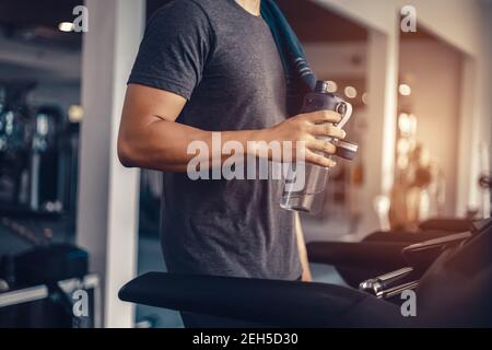 Un uomo in corsa sul tapis roulant in palestra e tenuta bottiglia d'acqua Foto Stock