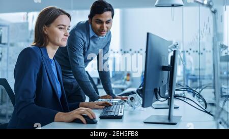 Modern Factory Office: Il supervisore del progetto maschile parla con un ingegnere industriale femminile che lavora al computer. Lavoro di squadra professionale, giovani specialisti Foto Stock