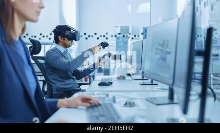 Fabbrica industriale moderna: Ingegnere meccanico che indossa cuffie per realtà virtuale, controller di tenuta, utilizza la tecnologia VR per la progettazione industriale Foto Stock