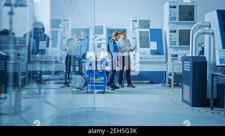 In officina: I lavoratori utilizzano macchinari CNC industriali ad alta tecnologia. Due professionisti della progettazione che parlano e utilizzano il tablet digitale. Foto Stock