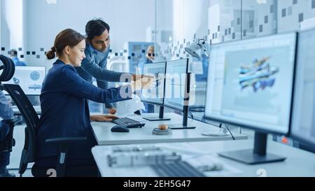 All'interno dell'ufficio di fabbrica: Il supervisore del progetto maschile parla con un ingegnere industriale femminile che lavora al computer, parla. In officina: Lavoratori professionisti Foto Stock