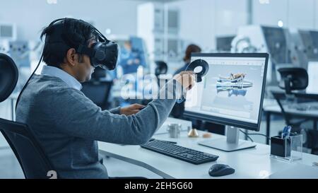 Fabbrica industriale moderna: Ingegnere meccanico che indossa cuffie per realtà virtuale, controller di tenuta, utilizza la tecnologia VR per la progettazione industriale Foto Stock