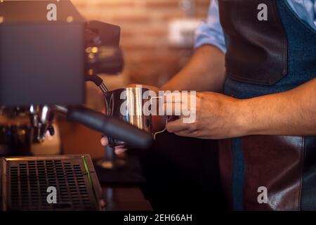 Barista che fuma il latte nella caraffa con macchina per il caffè per preparare la preparazione di latte art Foto Stock