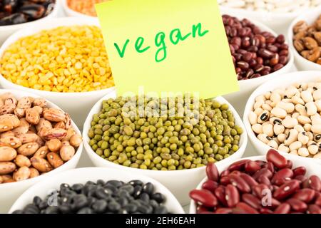 La raccolta di diversi fagioli e piselli nelle ciotole in ceramica con avviso vegano. Foto Stock