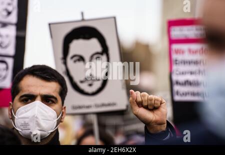 19 febbraio 2021, Hessen, Hanau: Un partecipante alla dimostrazione allunga dimostrativamente il suo pugno clenched verso l'alto davanti ad un poster con il ritratto di una delle vittime. Un'alleanza di organizzazioni giovanili di Hanau sotto il motto 'Nessun perdono - non dimenticare - insieme contro il razzismo' dimostra sulla piazza del mercato al monumento dei Fratelli Grimm. Una commemorazione congiunta degli assassini perpetrati nel gennaio 2020 dallo Stato dell'Assia e dalla città di Hanau si svolge nella città di Grimm, alla presenza del Presidente federale. L'assassino Tobias R. aveva sparato nove persone con un migrato Foto Stock