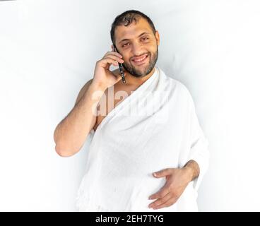 Uomo musulmano che fa una telefonata mentre indossa abiti da pellegrinaggio Foto Stock
