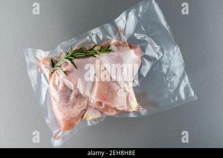 Cosce di pollo e rosmarino in sottovuoto confezionato sigillato per cottura sous vide, su fondo grigio Foto Stock