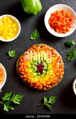 Arcobaleno veggie peperoni pizza campana su fondo di pietra nera. Vegetariano vegano o concetto di cibo sano. Piatto dietetico senza glutine. Vista dall'alto, disposizione piatta Foto Stock