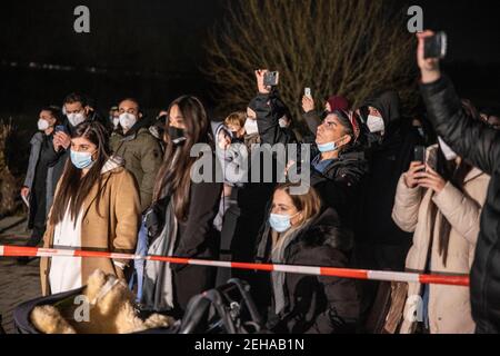 19 febbraio 2021, Hessen, Bruchköbel: Di fronte a un bar di narghilè a Bruchköbel, vicino Hanau, un gruppo di persone si riunì per commemorare l'omicidio razzista nell'anniversario dell'attacco ad Hanau. Le facce delle persone assassinate sono state proiettate sulla parete esterna del bar con graffiti e un'installazione leggera. Un estremista di destra aveva sparato nove persone ad Hanau il 19 febbraio 2020 per motivi razzisti. Successivamente, l'uomo aveva sparato sua madre e poi se stesso. L'atto ha causato orrore in tutto il mondo. Foto: Helmut Fricke/dpa Foto Stock