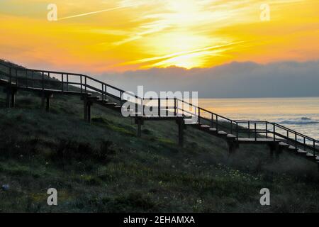 La sagoma ombreggiata di una scala di legno dal lato che conduce dal suolo nel cielo al tramonto e nello sfondo sfocato l'oceano, hor Foto Stock