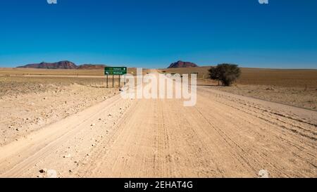 Viaggio su strada in Namibia - washboard su strada senza fine in ghiaia diritta Nelle pianure di Namib Naukluft Park - intersezione di due strade ghiaiose - strada verde sig Foto Stock